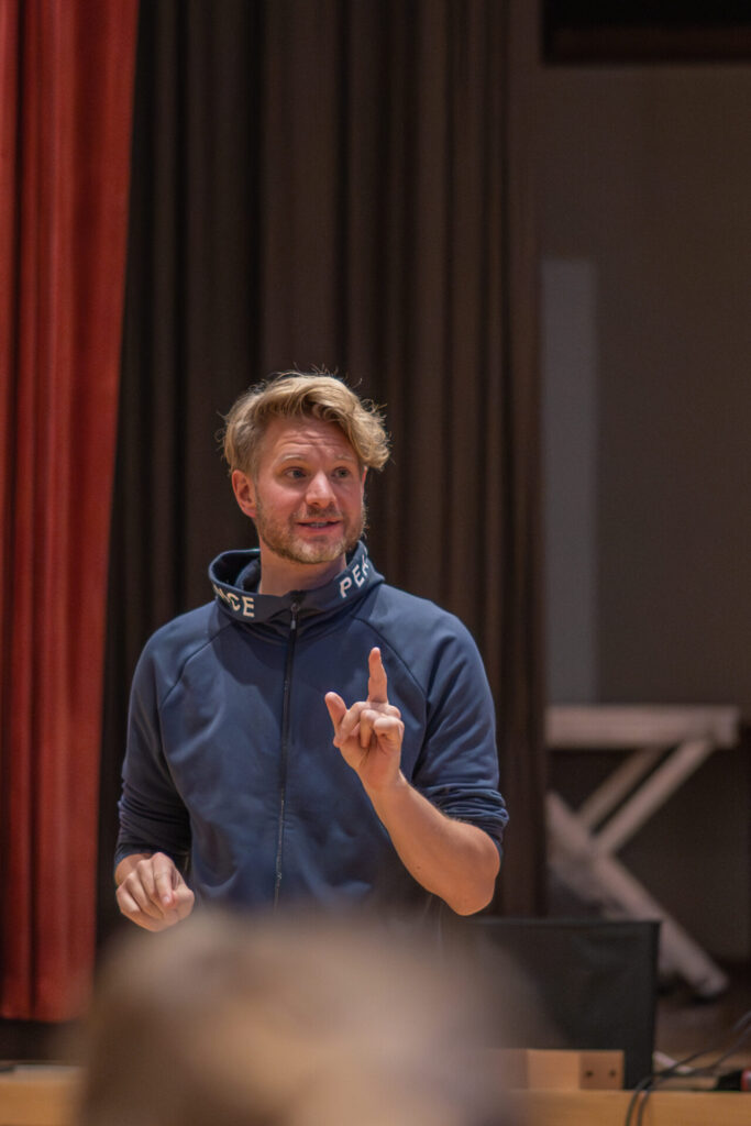 Matthias Bäuerlein gibt musikalische Anweisungen während der mobilen Choraufnahme im Gemeindesaal von St. Vigil für das Weihnachtsalbum „Send Jesus Today“. Foto: Gianvito Coco